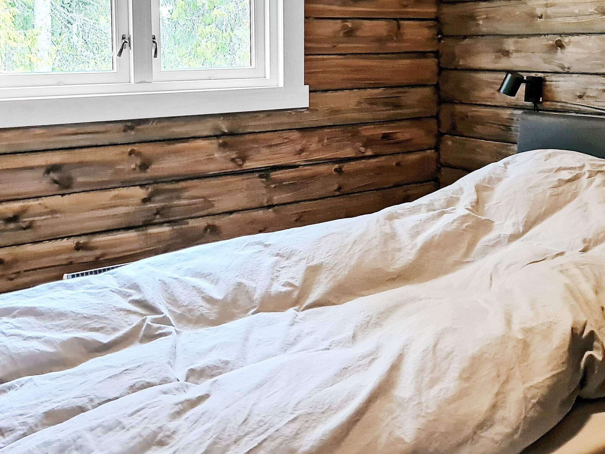 Een houten kamer met een bed, een raam en een nachtkastje.