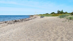 A gravel beach with a clear sky and distant wind turbines.