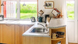 A kitchen with a sink, kettle, coffee maker, and a shelf with mugs and a plate.