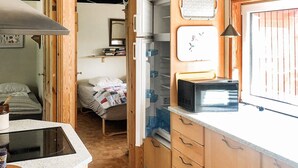 A compact kitchen with a microwave, a small refrigerator, and a stove. There is a bed in the adjacent room.