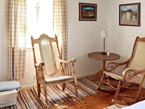 Relax in a serene space with a traditional chair, matching rocking chair, and a small table with a candle and lamp.