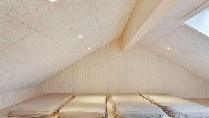 A high-ceilinged room with wooden walls and a sloped ceiling, featuring a large bed with multiple pillows and a wooden floor. - Holiday Home in Juelsminde (Juelsminde)