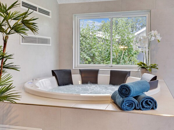 A spa room with a hot tub, a window with a view of greenery, and a potted orchid.
