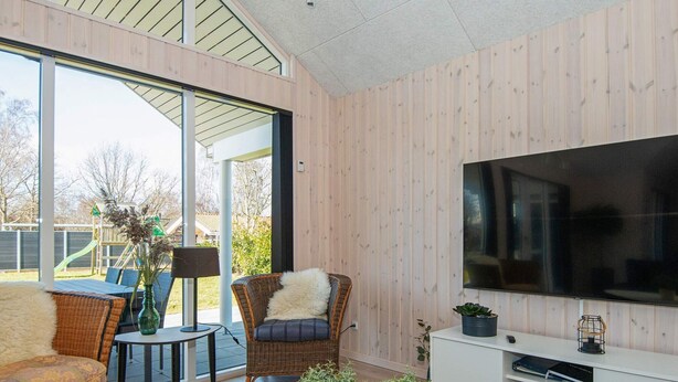 A modern living room with a large TV, wicker furniture, and a view of a playground. - Holiday Home in Juelsminde (Juelsminde)