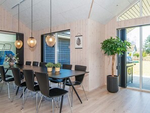 A modern dining area with a long table, black chairs, and hanging pendant lights.