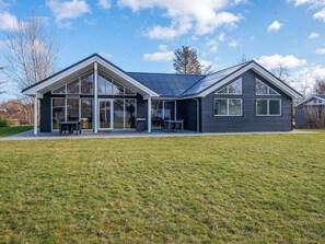 A modern house with a large glass front, a covered patio, and a solar panel roof. - Holiday Home in Juelsminde (Juelsminde)