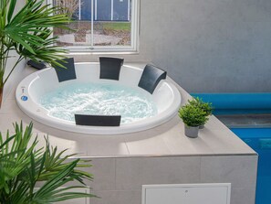 A hot tub with a built-in seat and controls, surrounded by a tiled area with a potted plant. - Holiday Home in Juelsminde (Juelsminde)