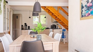 A modern kitchen with a wooden staircase, a dining table with chairs, and a hanging pendant light.