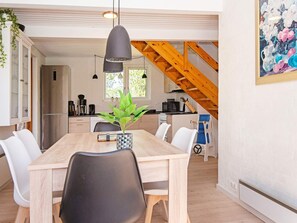 A modern kitchen with a wooden staircase, a dining table with chairs, and a hanging pendant light.