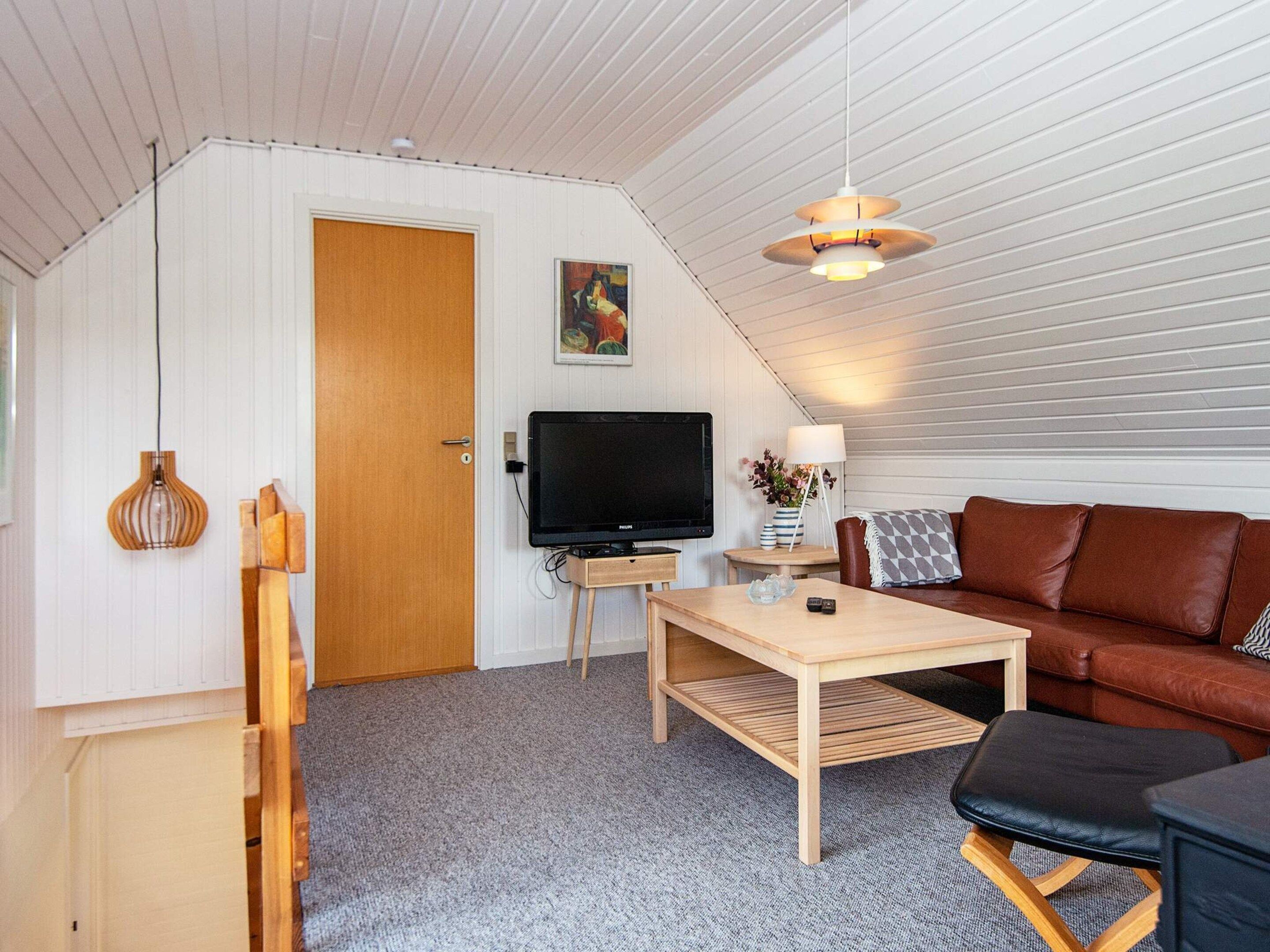 Une pièce confortable avec une télévision, une table basse en bois, un canapé en cuir marron et un ventilateur de plafond.