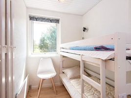 Habitación con literas, ventana, radiador y una silla blanca.