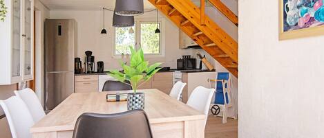 A modern kitchen with a wooden ceiling, a dining table with chairs, and a hanging pendant light.