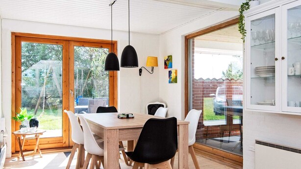 A dining area with a wooden table, white chairs, black pendant lights, and a view through glass doors to the outdoors. - 6 Person Holiday Home in Glesborg (Glesborg)