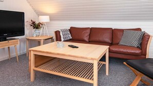 A modern living room with a brown leather sofa, a wooden coffee table, a TV on a stand, and a lamp on a side table. - 6 Person Holiday Home in Glesborg (Glesborg)