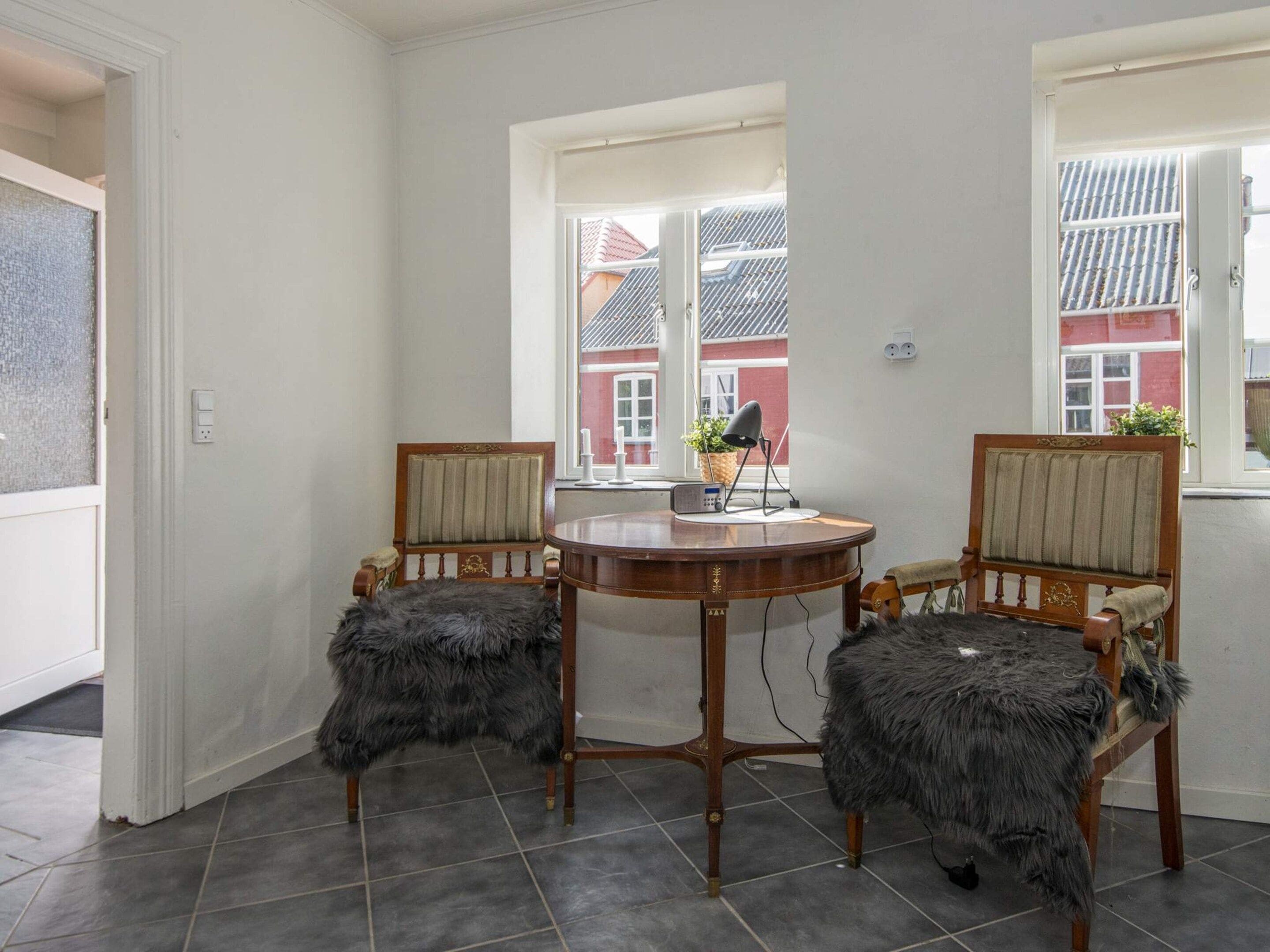 Una habitación con una mesa redonda de madera, dos sillas con asientos de piel y una lámpara, además de un ventanal con vistas a edificios.