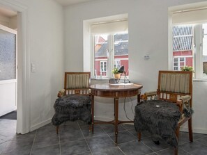 A room with a round wooden table, two chairs with fur throw seats, a lamp, and a window with a view of buildings. - 6 Person Holiday Home in Bredebro (Bredebro)
