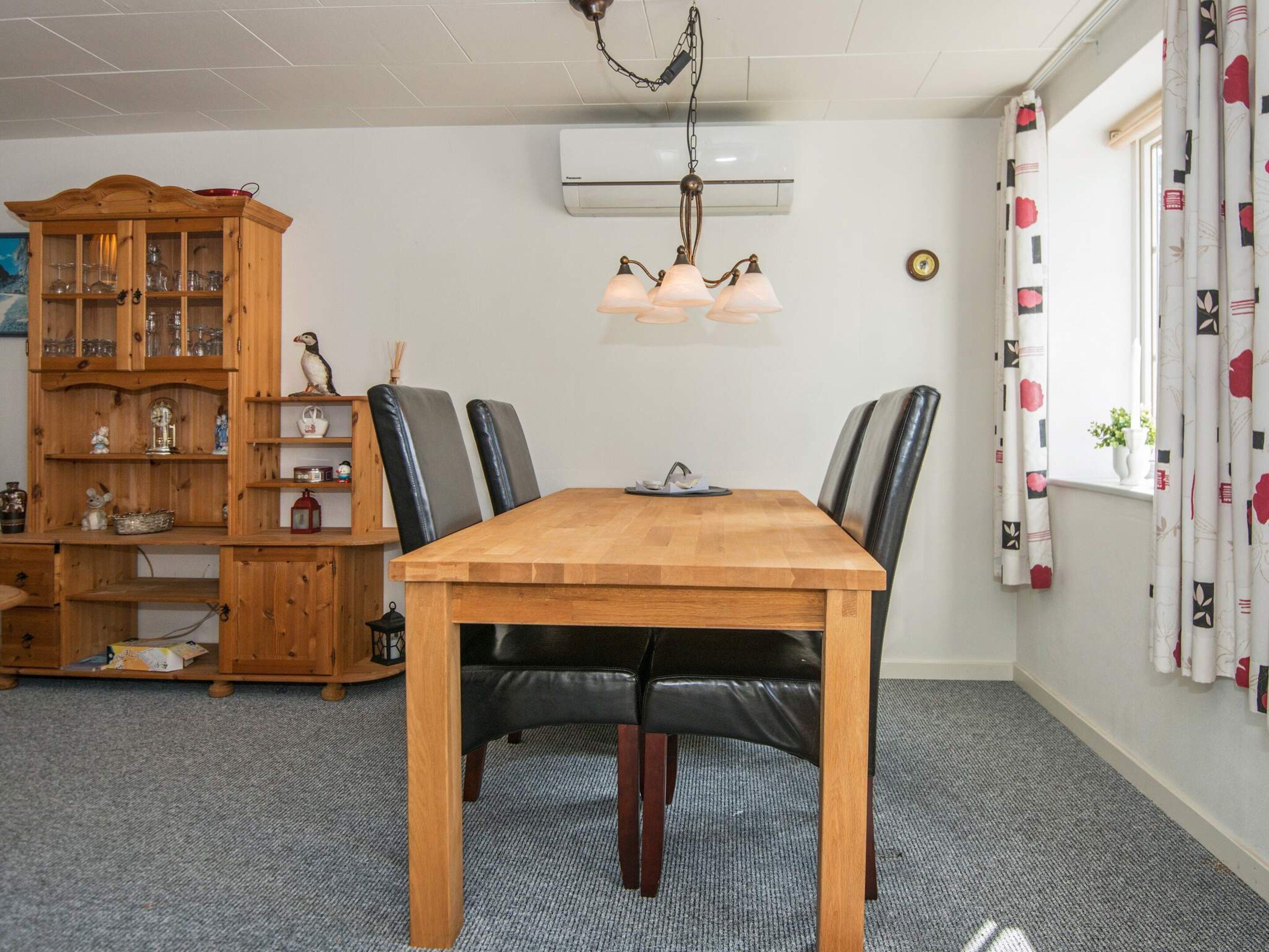 Ein Essbereich mit Holztisch, schwarzen Ledersesseln, einem Holzkabinett mit Glastüren und einer Deckenleuchte.