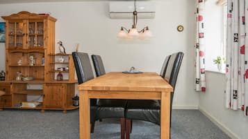 Ein Essbereich mit Holztisch, schwarzen Ledersesseln, einem Holzkabinett mit Glastüren und einer Deckenleuchte.
