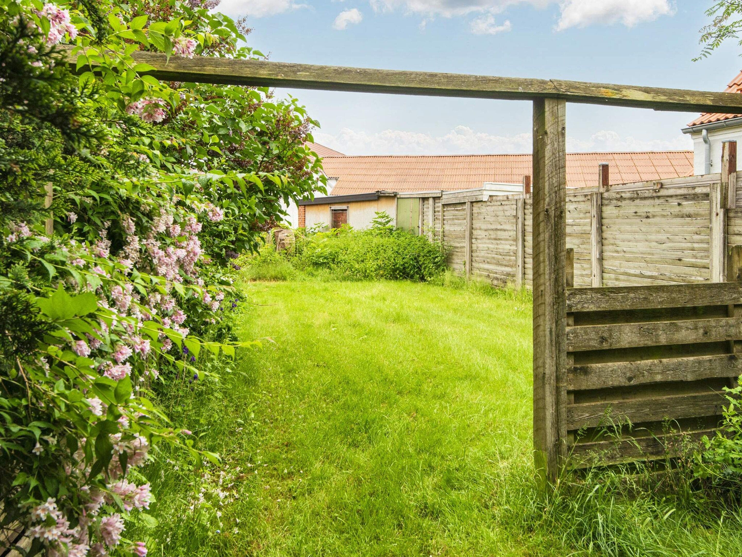 Eine hölzerne Pergola in einem Garten mit Rasenfläche und einem Backsteinhaus im Hintergrund.