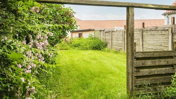 Eine hölzerne Pergola in einem Garten mit Rasenfläche und einem Backsteinhaus im Hintergrund.