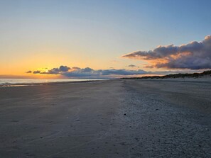 En strand med solnedgang, sandet bredde og klitter i baggrunden.