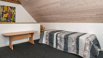 Ein kleiner, gemütlicher Raum mit schrägen Wänden, einer hölzernen Bank, einem Bett mit einem gemusterten Bettdeckchen und einem farbenfrohen, abstrakten Gemälde an der Wand.