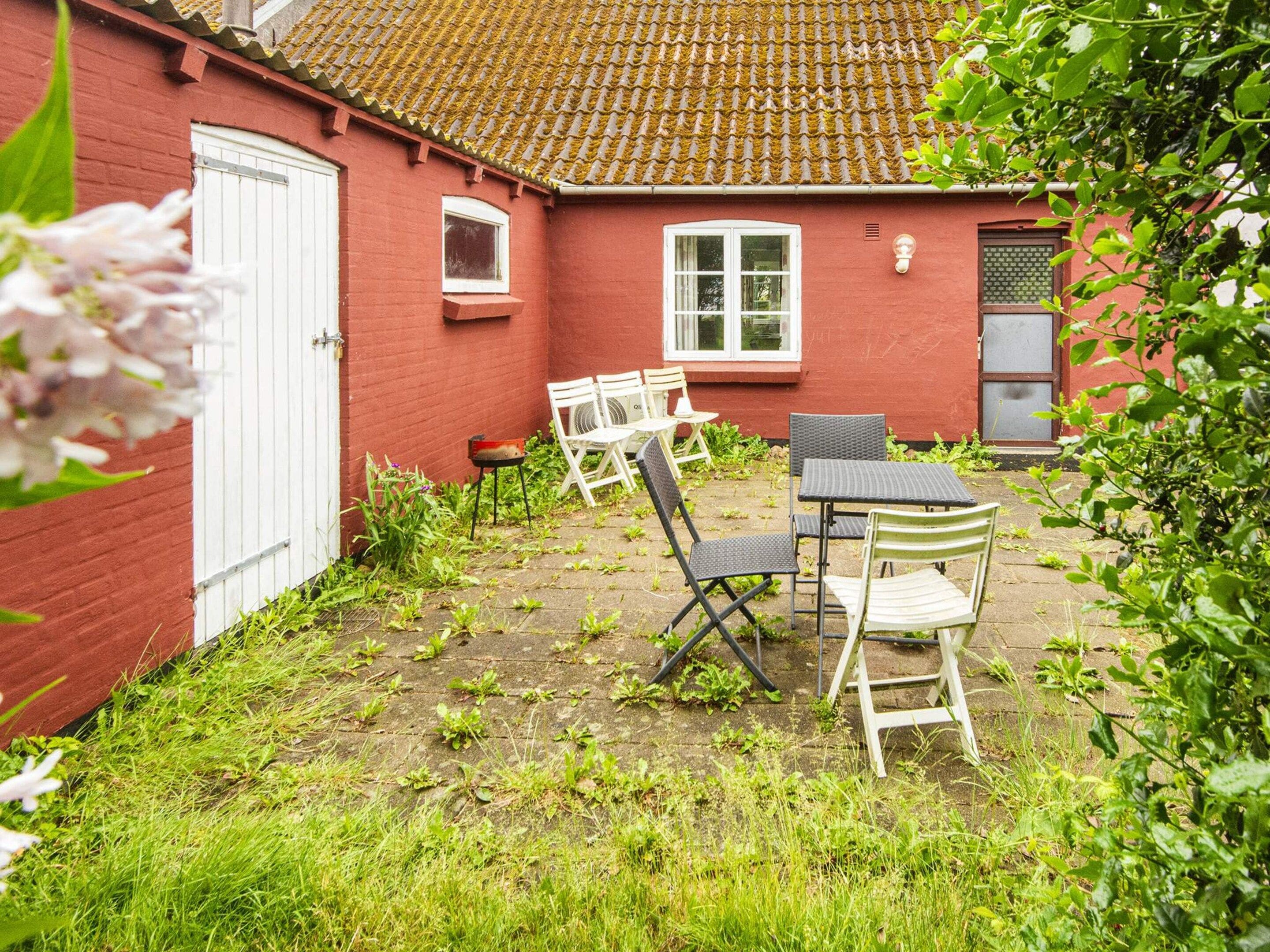 A red brick house with a tiled roof, a white door, and a small patio with outdoor furniture.