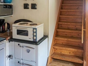 A kitchen with a microwave oven on top of a stove, wooden cabinets, and a wooden staircase. - 4 Person Holiday Home in Olofstrom (Olofström)
