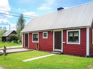 Une maison en bois rouge avec un toit en métal, une porte d’entrée et des fenêtres.