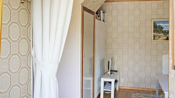 Quarto com teto de madeira, porta branca, mesa pequena com abajur e parede estampada.