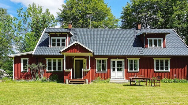 A red wooden house with a grey roof, a front porch, and a small garden area.