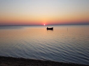 Água calma com um barco ao longe e um pôr do sol.