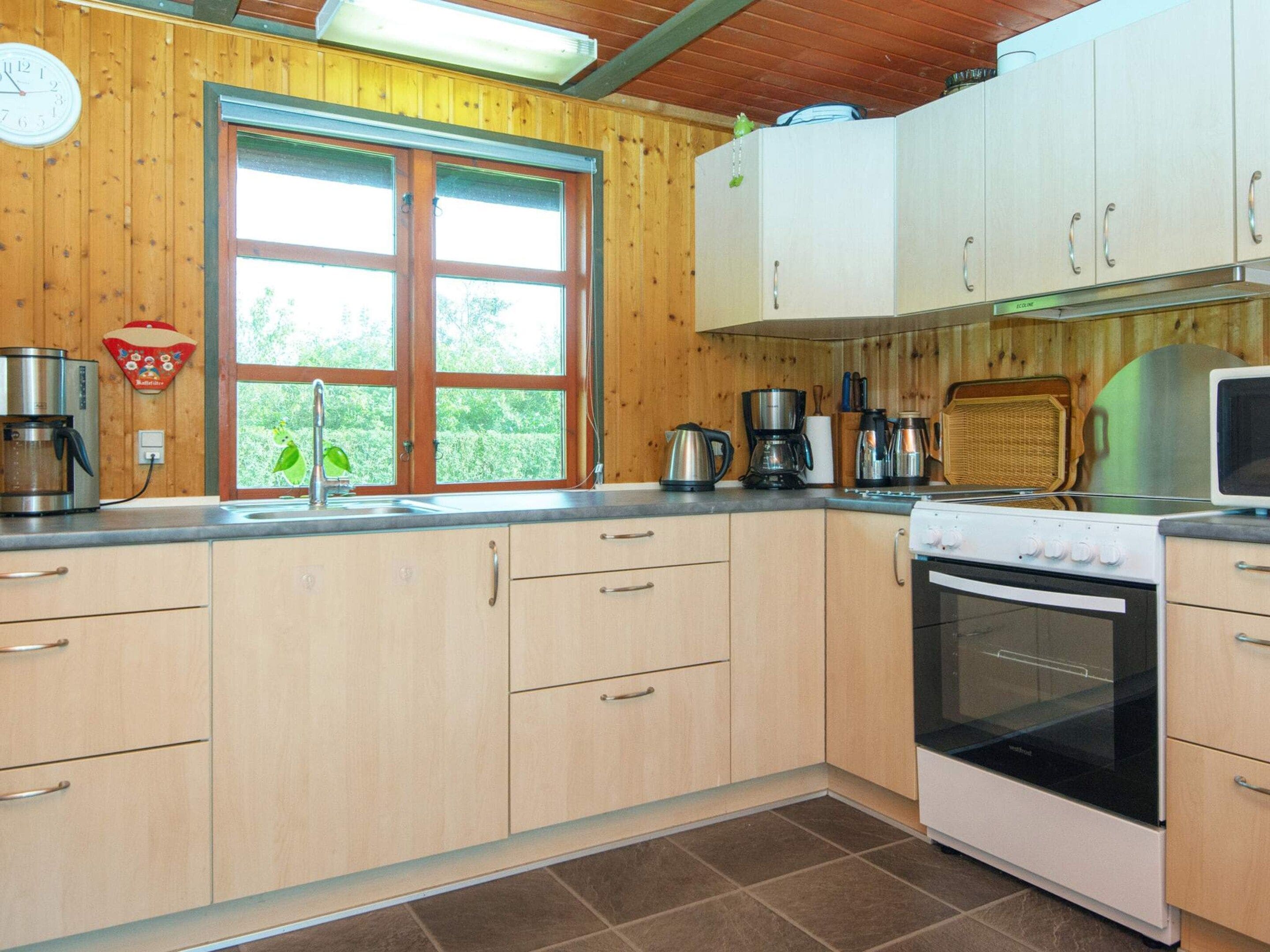 Cocina con gabinetes de madera, estufa y ventana con vista a follaje.
