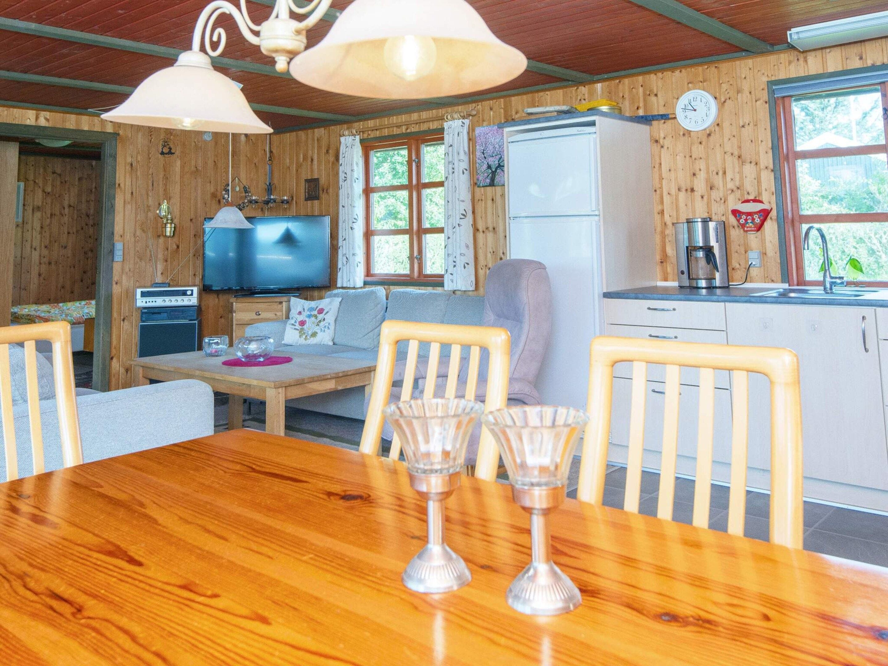 Interior acogedor de una cabaña con una mesa de comedor de madera, sillas, un sofá, un televisor, un refrigerador y una zona de cocina.