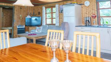 Interior acogedor de una cabaña con una mesa de comedor de madera, sillas, un sofá, un televisor, un refrigerador y una zona de cocina.