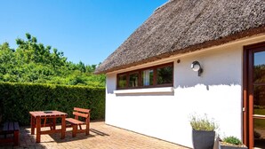 A white building with a thatched roof, a patio with a table and chairs, and a large planter. - Holiday Home in Aars (Aars)