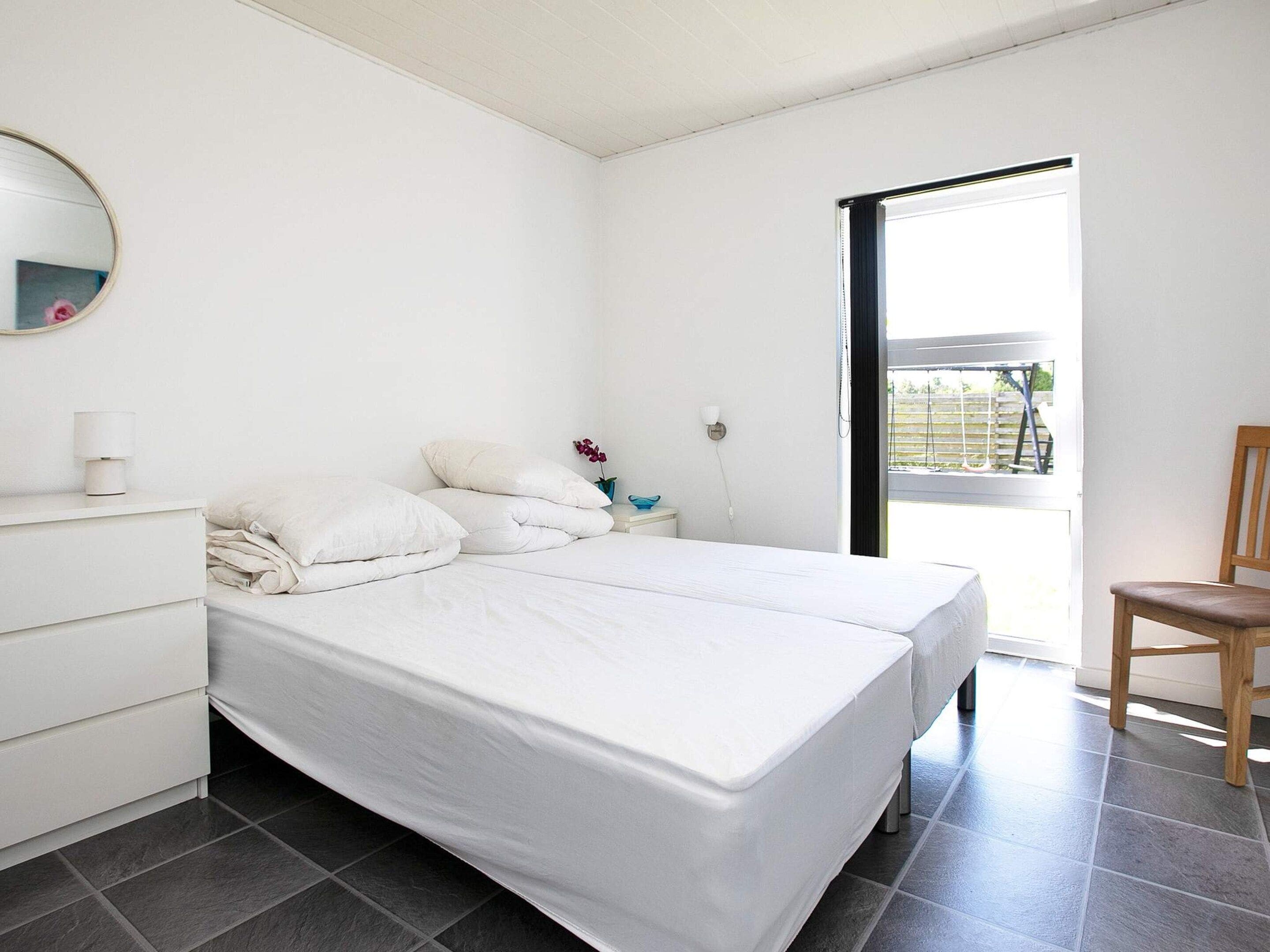 Una camera da letto con un letto, un comodino, una lampada, uno specchio e una sedia.