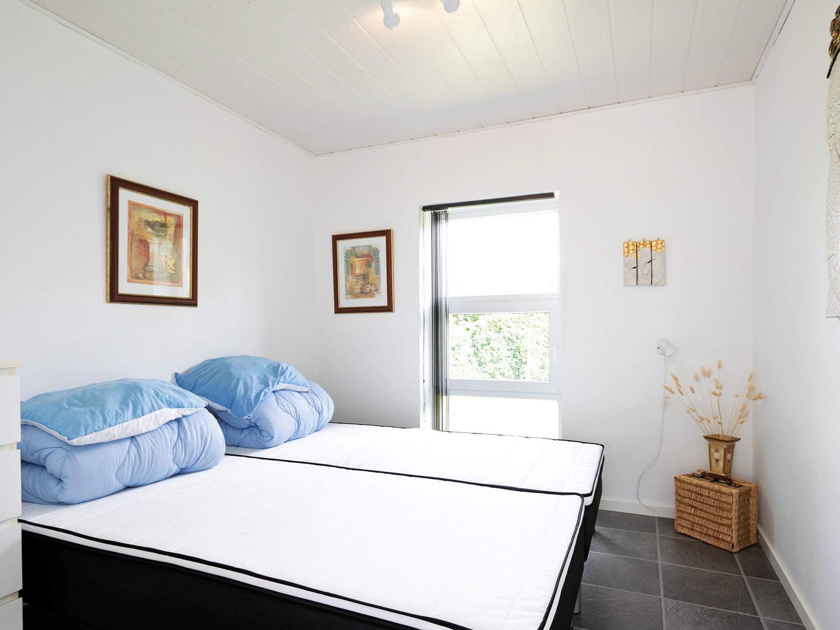 Un dormitorio con una cama, dos cuadros enmarcados, un ventanal y una lámpara de noche.