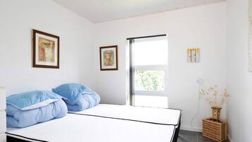 Un dormitorio con una cama, dos cuadros enmarcados, un ventanal y una lámpara de noche.