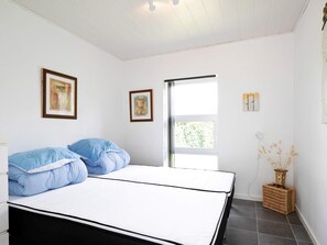 A bedroom with a bed, two framed pictures, a window, and a bedside lamp.