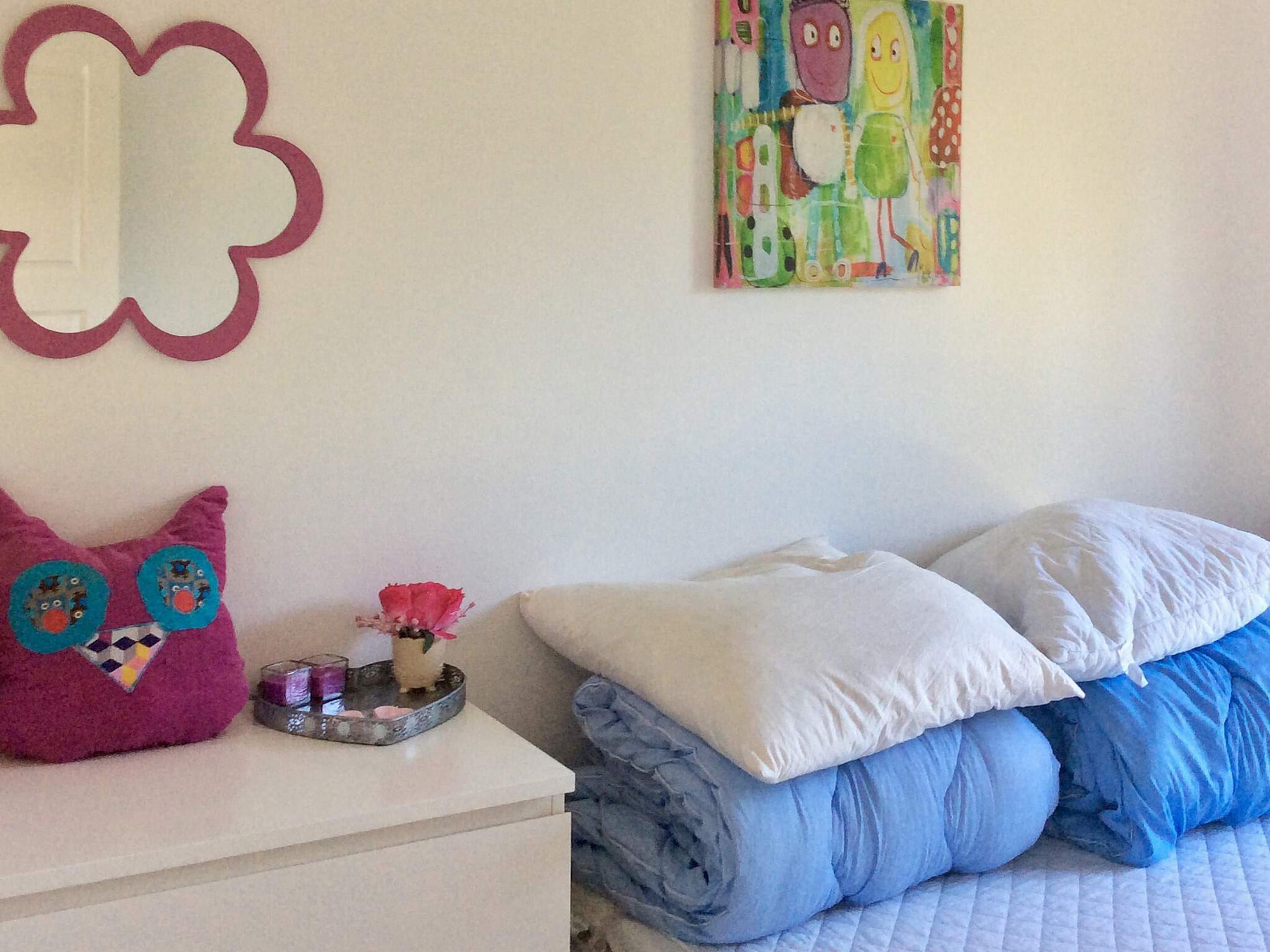 A bedroom with a bed, pillows, a dresser, a mirror, and a wall decoration.