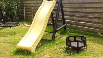 A playground with a yellow slide, a swing set, and a round black play structure.