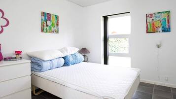 Ein Schlafzimmer mit einem Bett, weißen Wänden und zwei farbenfrohen Bildern.