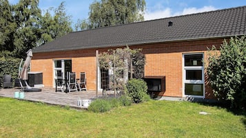 A brick building with a tiled roof, a patio with outdoor furniture, and a grassy yard.