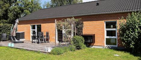 A brick building with a tiled roof, a patio with outdoor furniture, and a grassy yard.