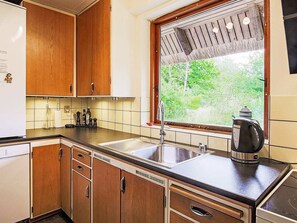 A kitchen with wooden cabinets, a stainless steel sink, and a window with a view of greenery.