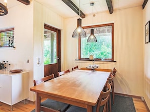 A dining area with a wooden table and chairs, a window with a view of greenery, and pendant lighting.