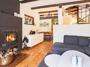 A cozy living room with a fireplace, a sofa, and a dining area with wooden flooring and a staircase.