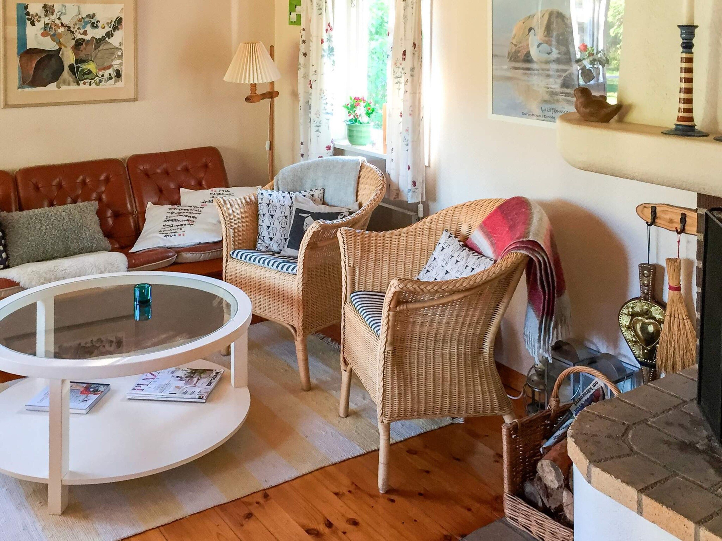 A cozy living room with a brown leather sofa, wicker chairs, a white coffee table, and a fireplace with decorative items.