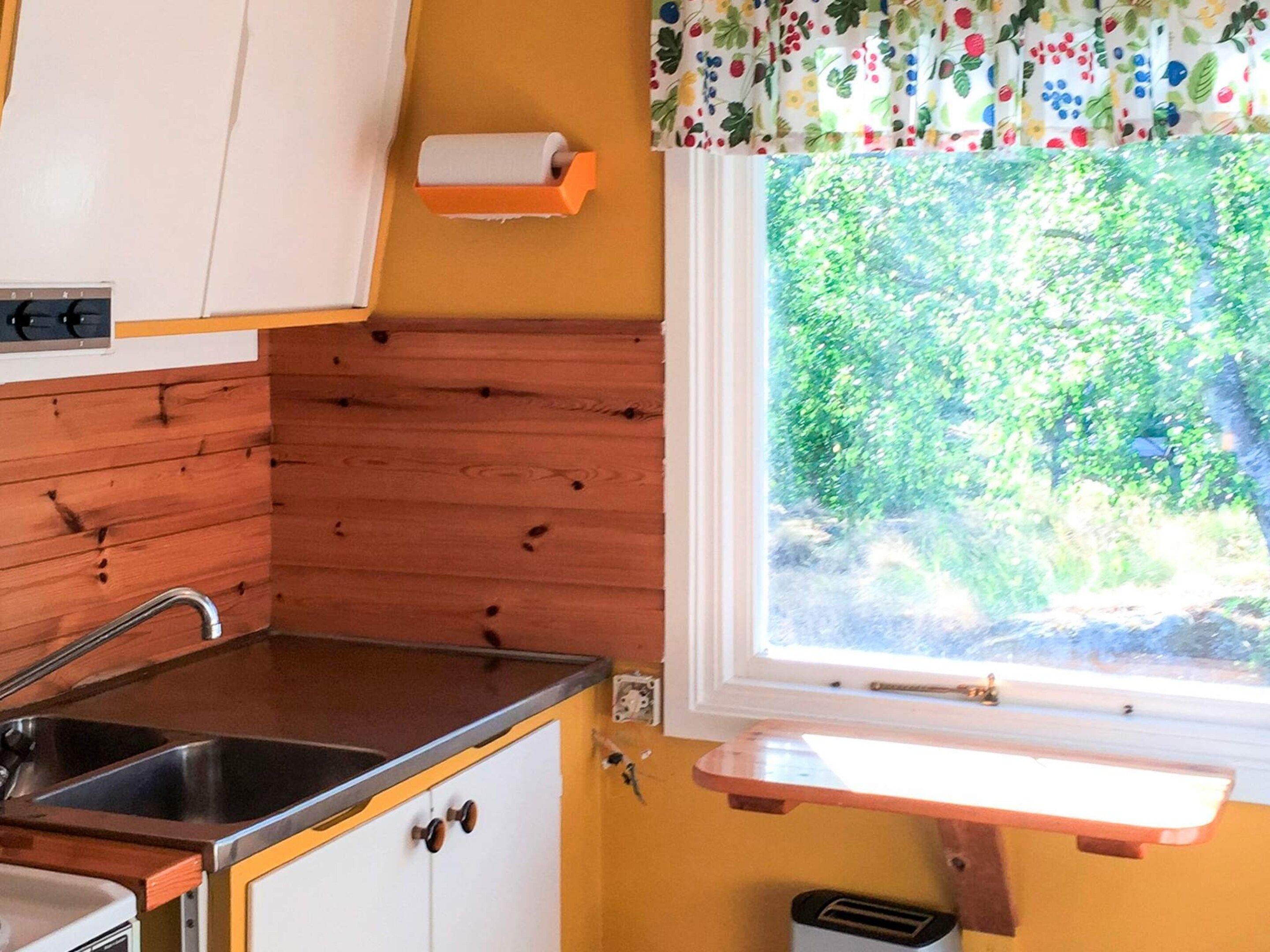 Kompakti keittiö, jossa on puiset kaapit, ruostumattomasta teräksestä valmistettu pesuallas ja ikkuna, josta avautuu näkymä vehreään maisemaan.